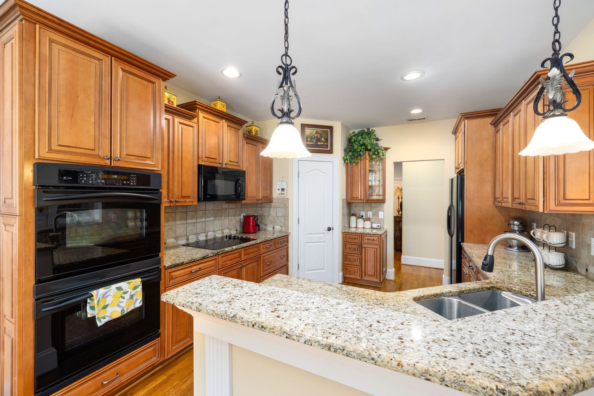 Bright kitchen with wood cabinets, granite island, black appliances, and a stainless steel fridge.