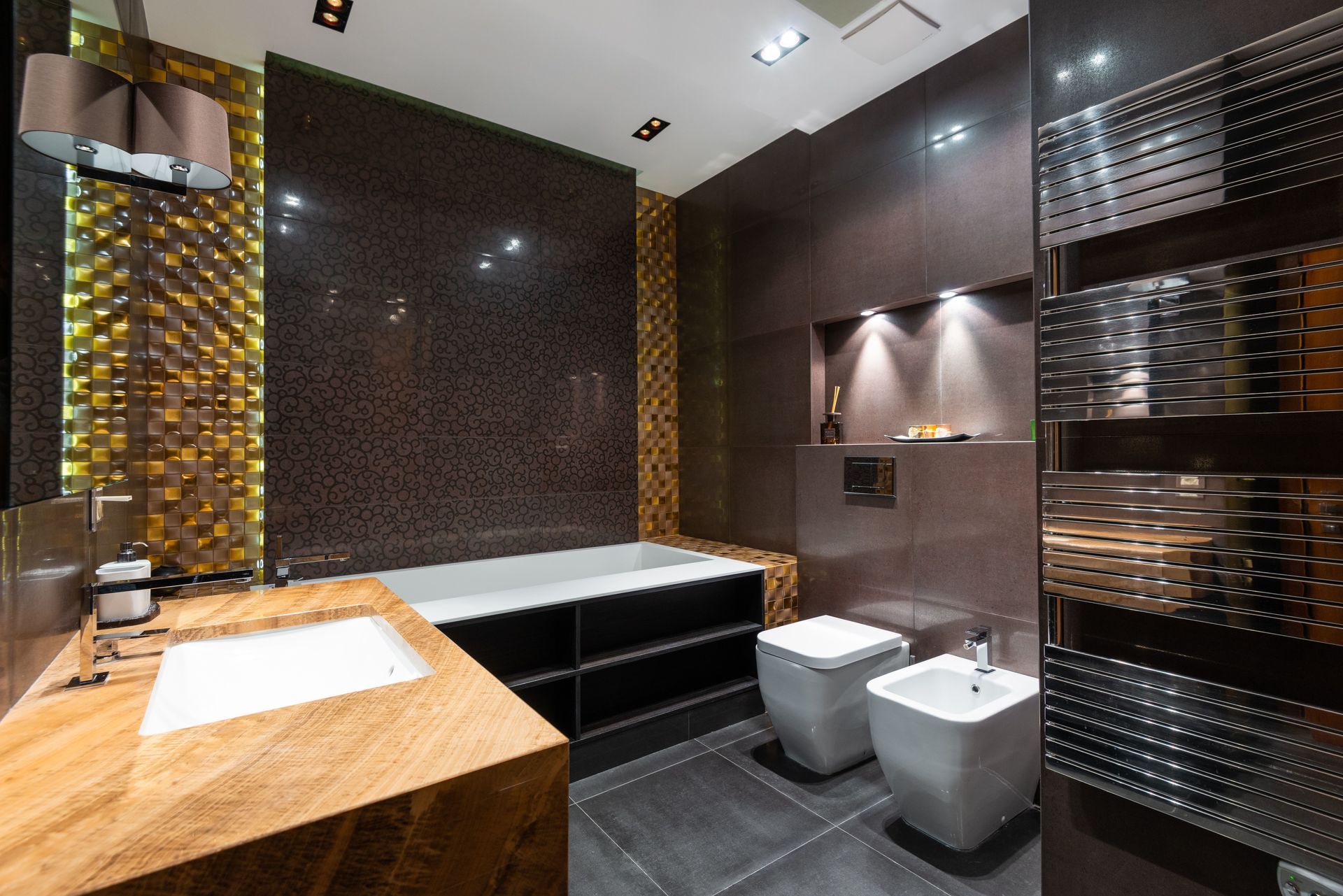Modern bathroom with a bathtub, two sinks, dark tiled walls, and warm lighting