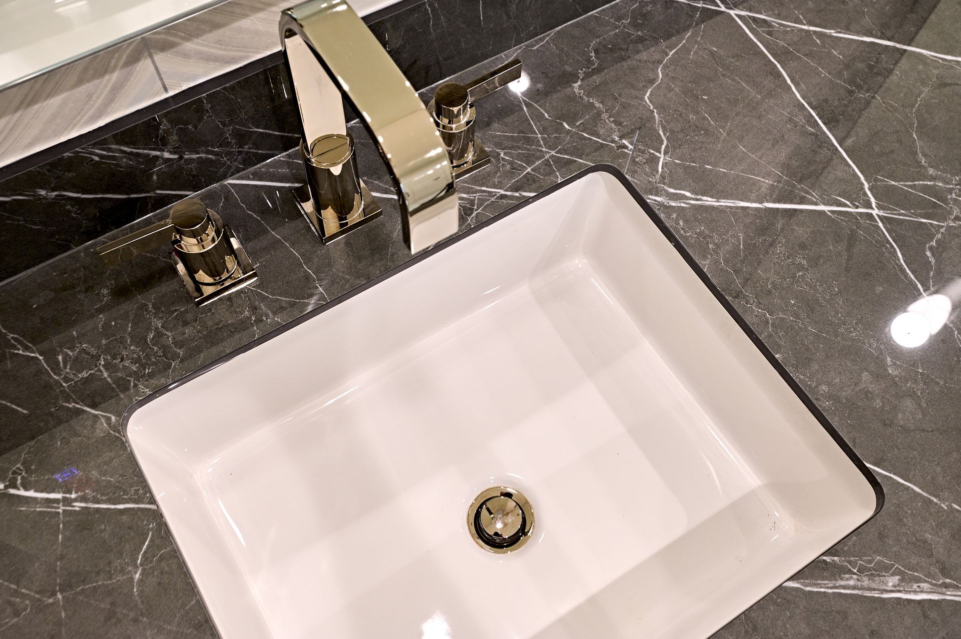 White rectangular bathroom sink with a gold faucet on a dark marble countertop