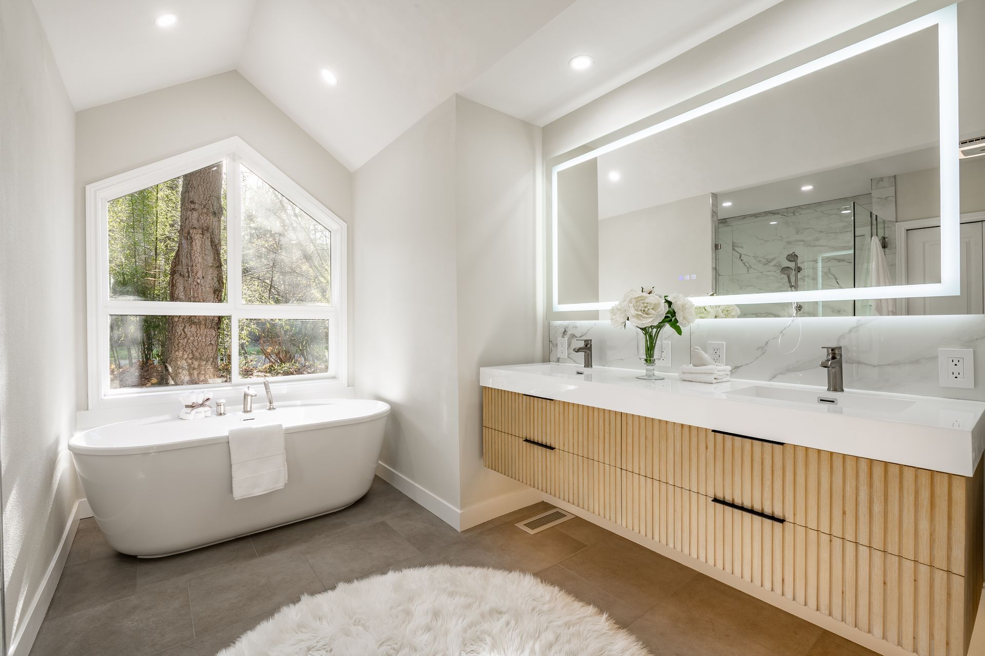 Bright modern bathroom with freestanding tub, large mirror, wood vanity, and skylight.
