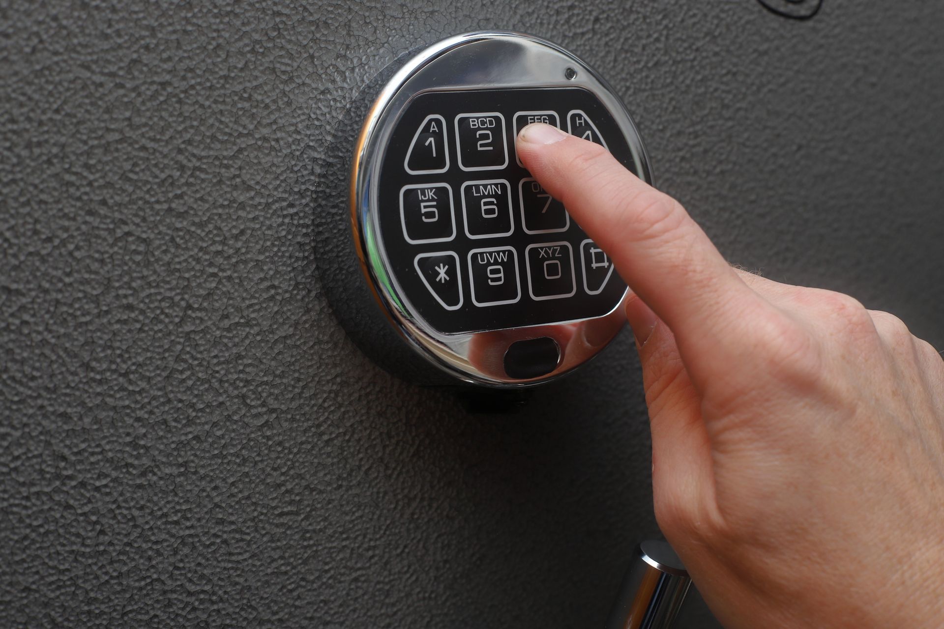 Hand entering code on electronic keypad lock of secure metal safe for valuables protection.