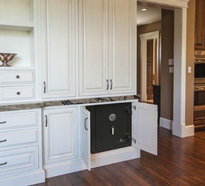 Black security safe installed in white cabinetry, with open doors revealing the combination dial. Set in a home kitchen.