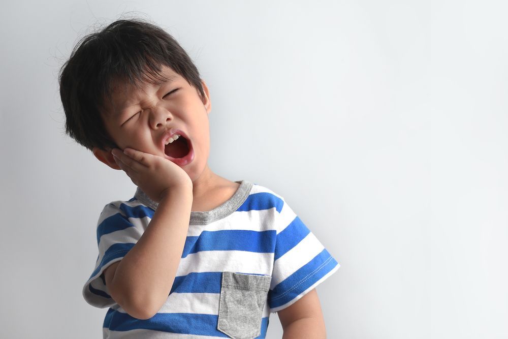 Child holding their cheek in tooth pain, indicating possible cavity or dental discomfort