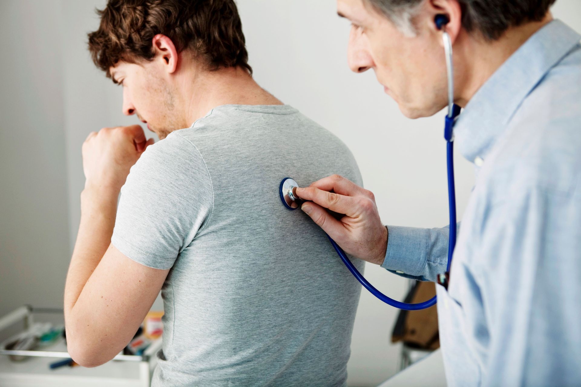 Médico auscultando as costas de paciente com estetoscópio durante consulta