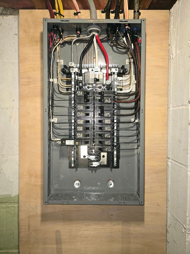 Open electrical breaker panel with exposed wiring and multiple circuit breakers mounted in a wall recess