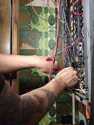 Person wiring a crowded electrical panel with red cables and tools in a narrow indoor space
