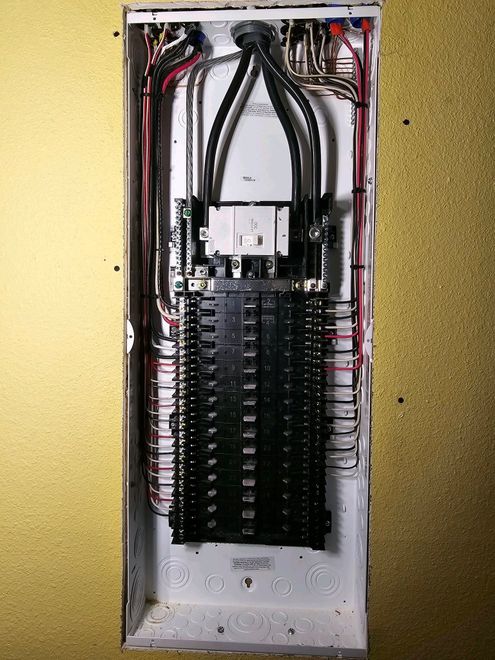 Open electrical breaker panel with wiring and circuit breakers inside a metal box