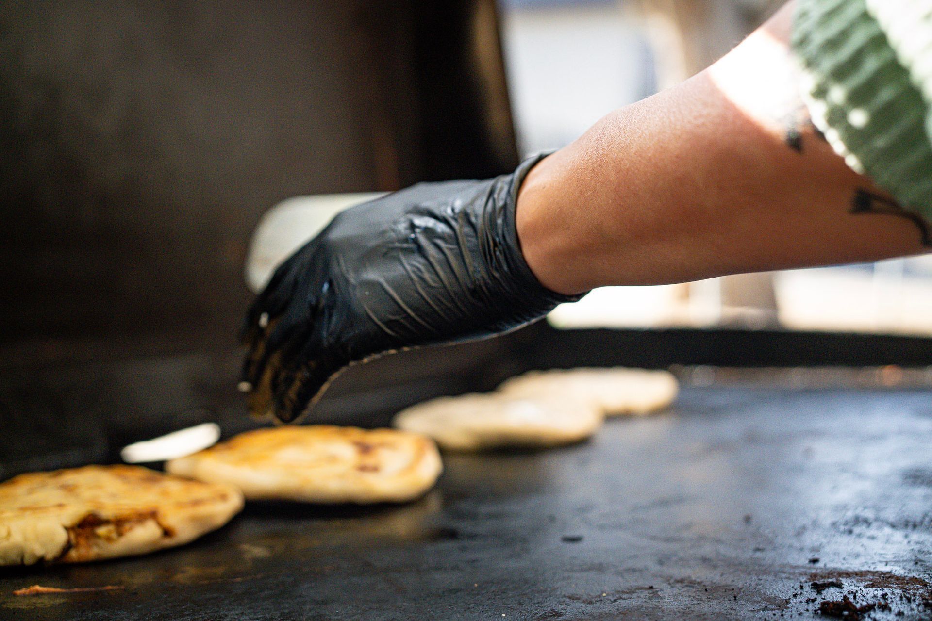 Person in black glove, grilling food on a flat top.