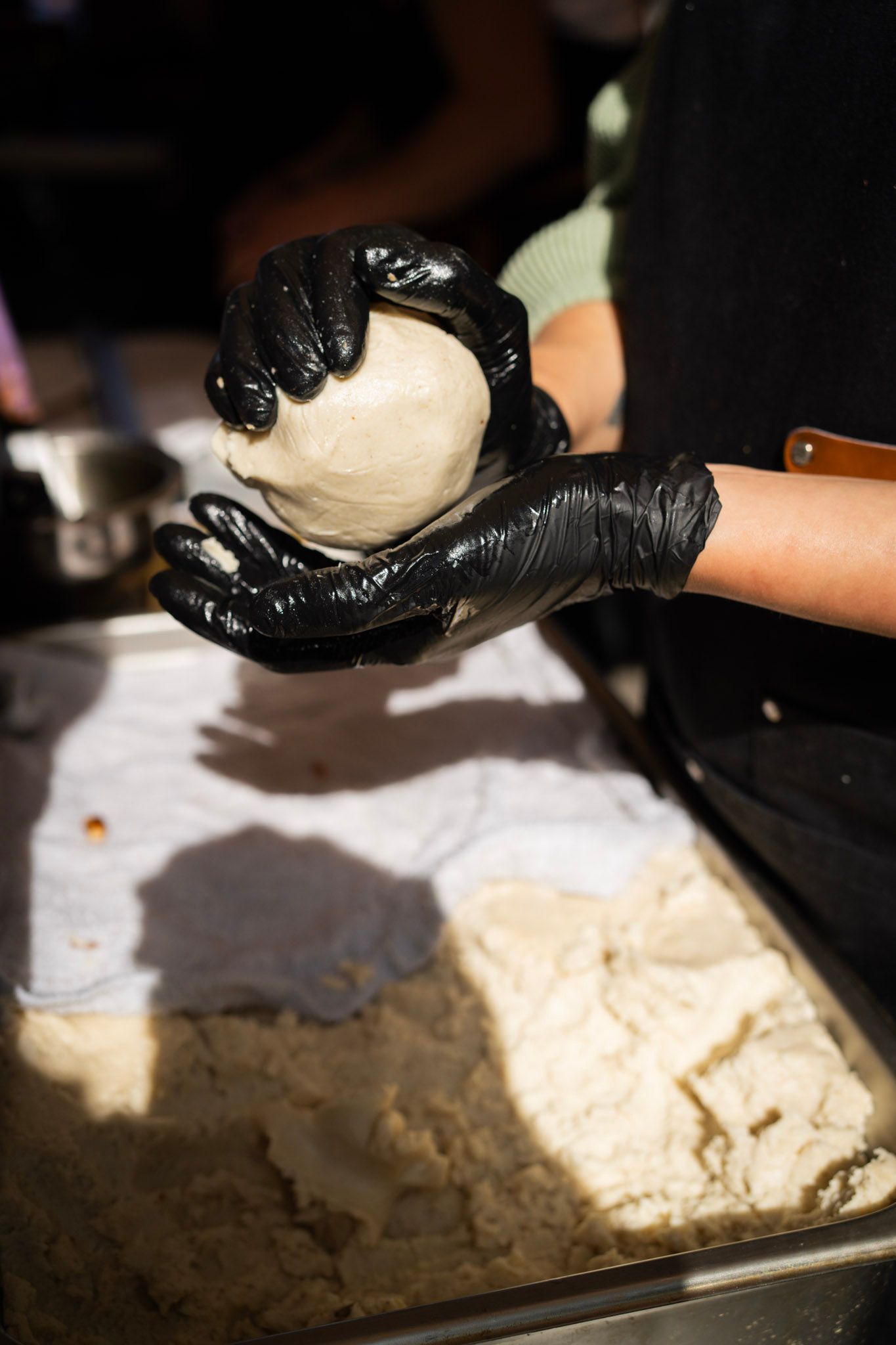 Person wearing black gloves shapes dough into a ball, near a tray of flour.