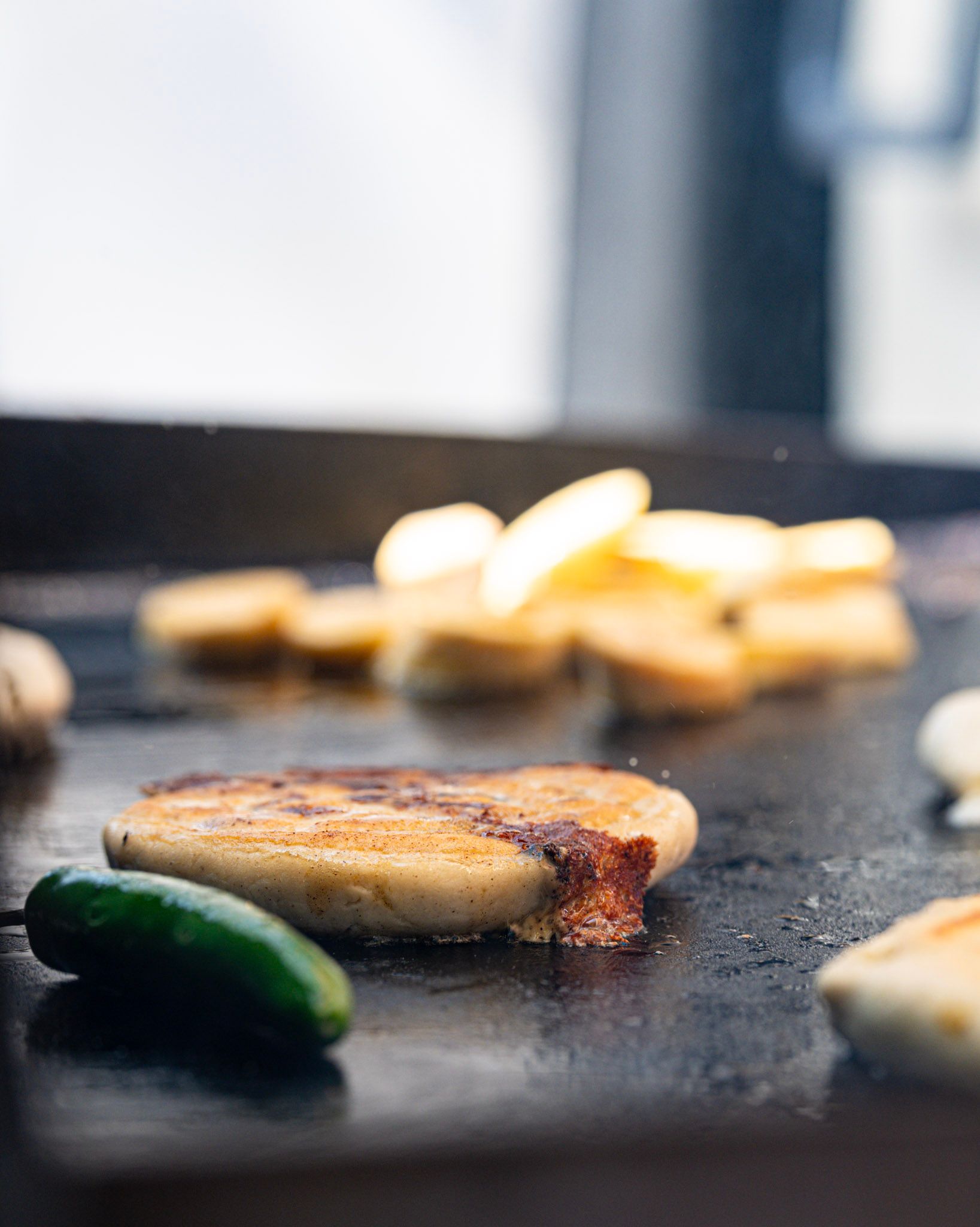 Sausage patty searing on a black griddle, with jalapeno and mushrooms, close up.
