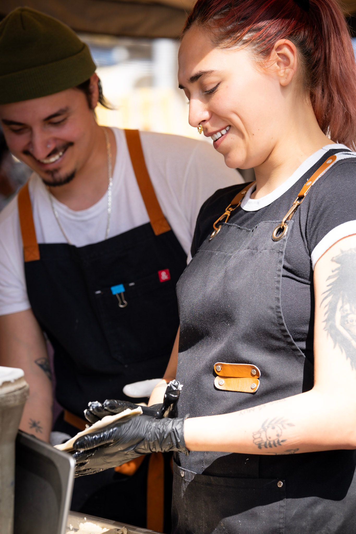 Two people in aprons preparing food, smiling.