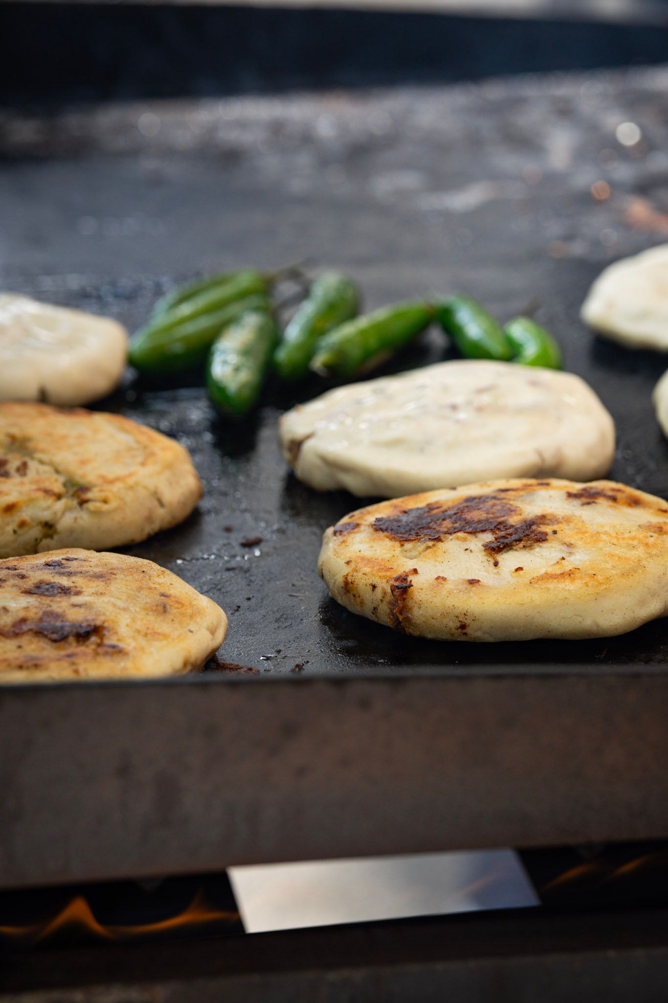 Flatbreads and jalapeños grilling on a flat top.