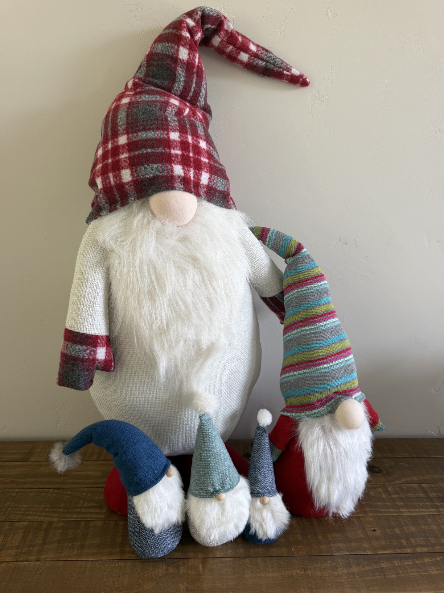 Holiday gnome figurine in a plaid hat and striped sleeves, standing on a table with two smaller gnomes.