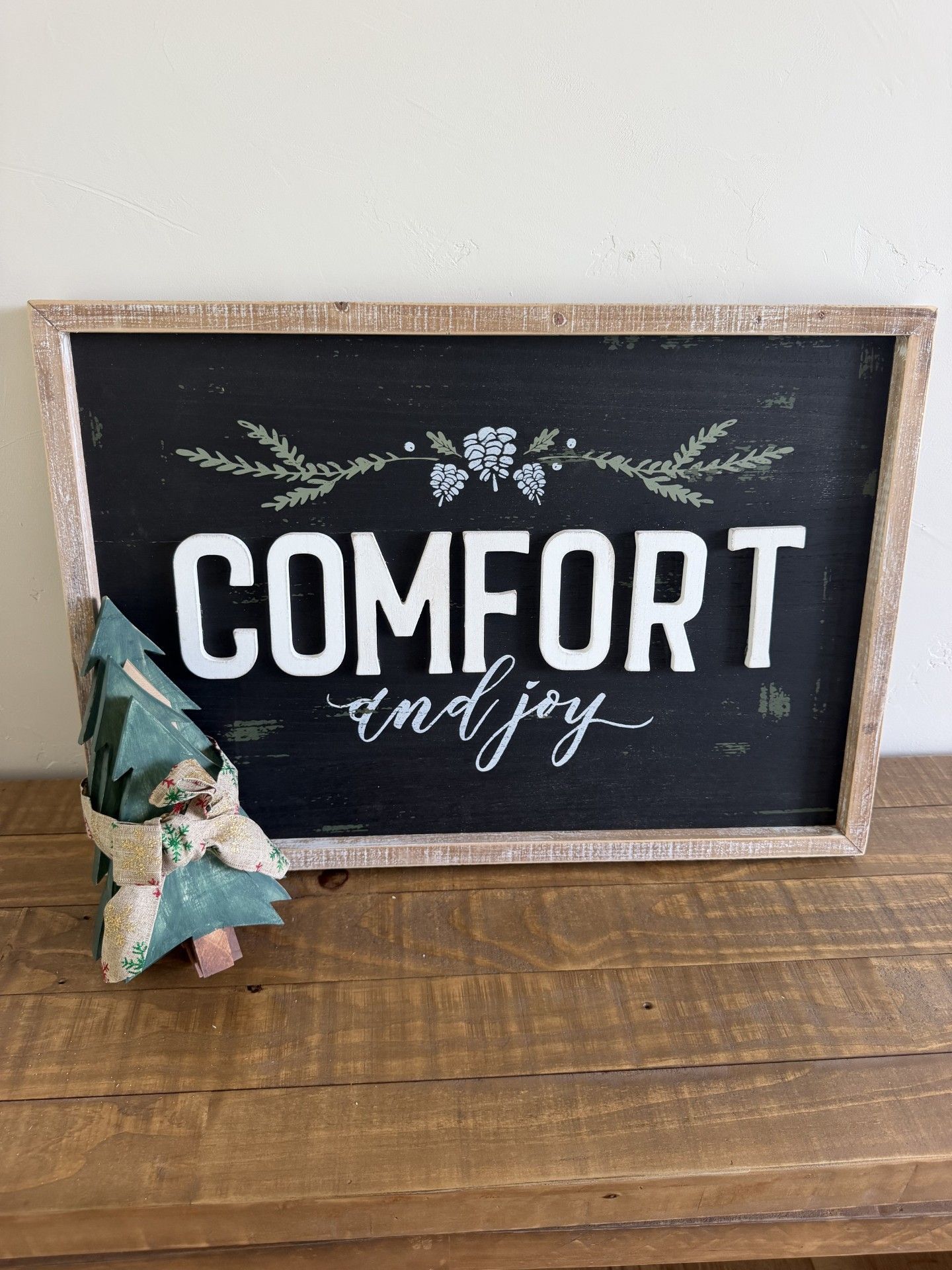Framed sign reading “COMFORT” on a rustic wooden surface with a small plant beside it