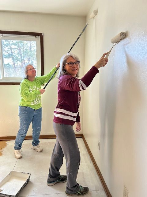 Two women are painting a wall with paint rollers