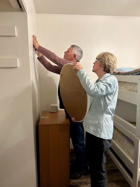 A man and a woman are measuring a wall in a bedroom.