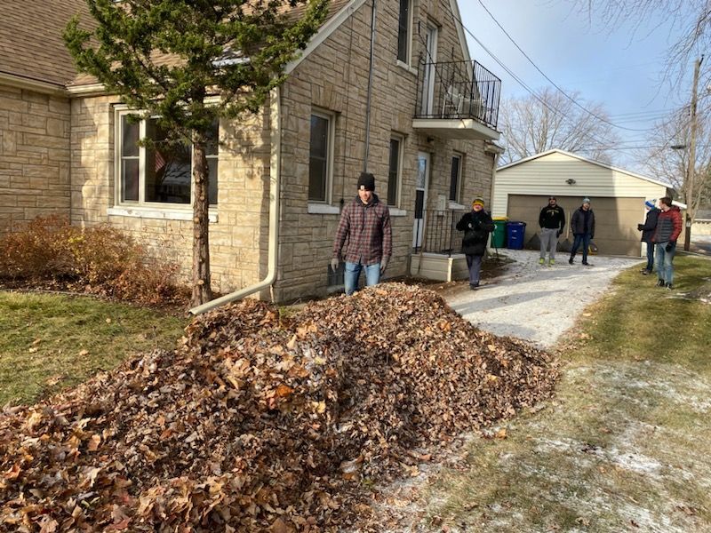 A group of people are standing next to a pile of leaves in front of a house.
