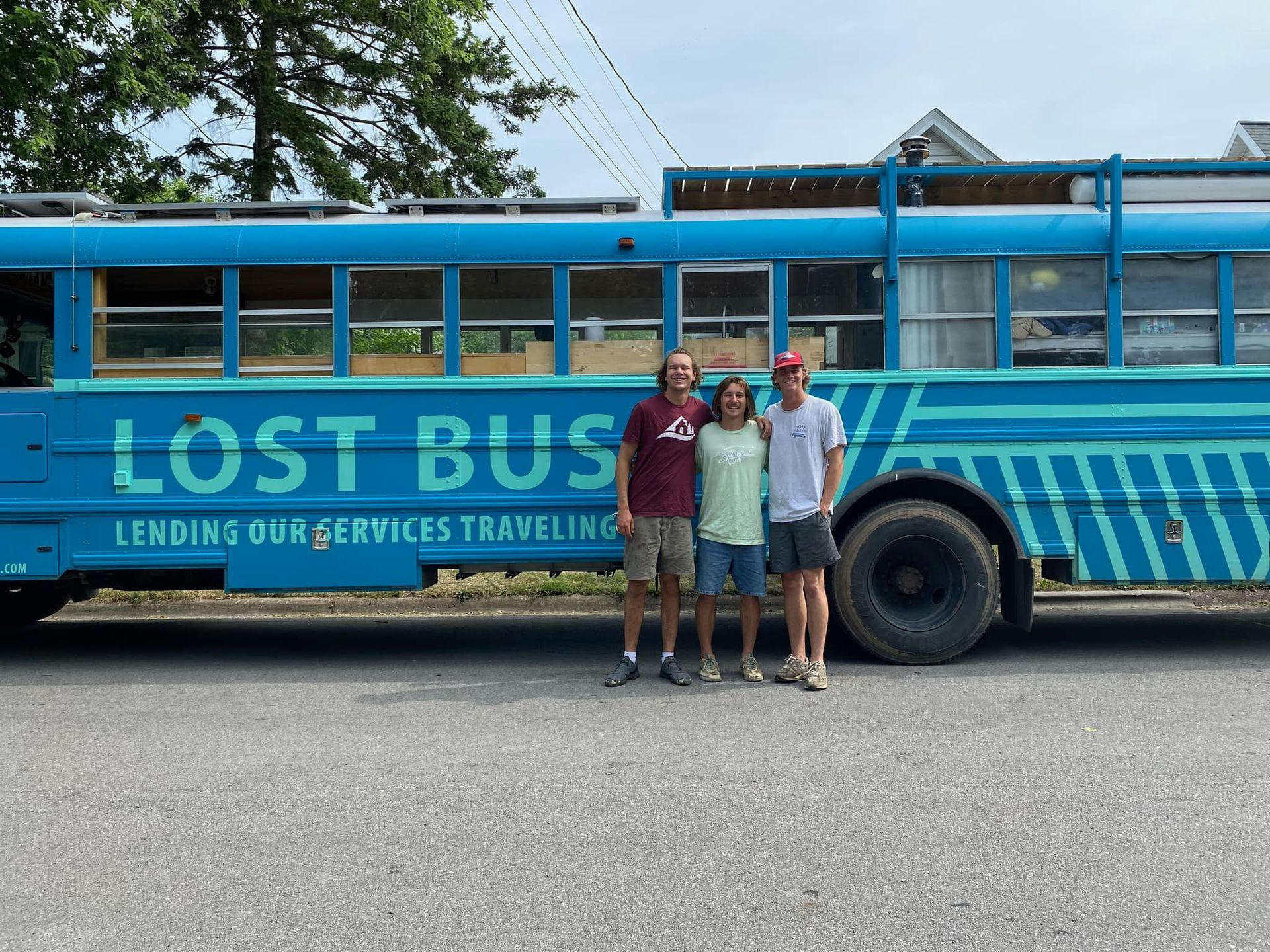Three people are standing in front of a blue bus that says lost bus lending our services traveling.