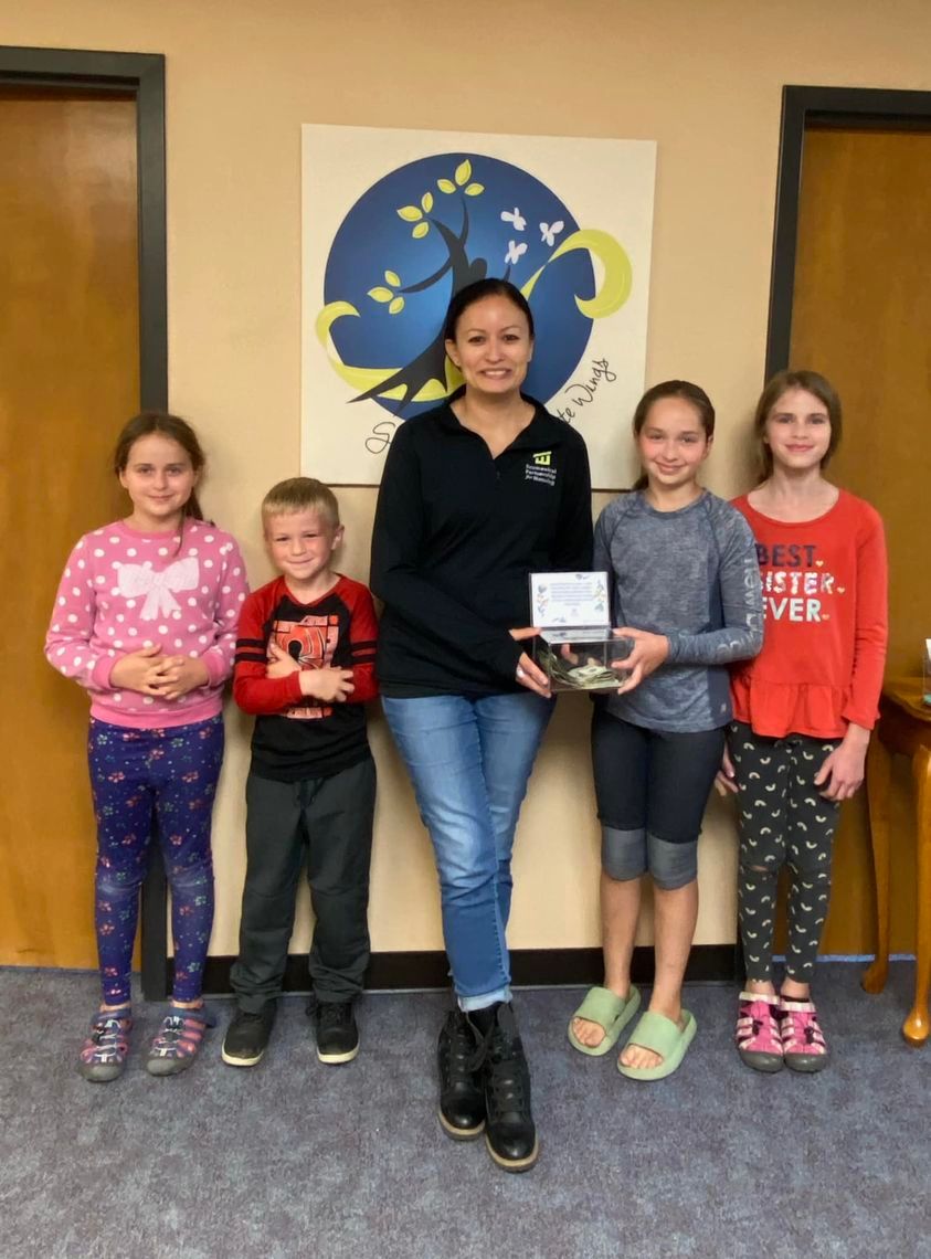 A group of children standing next to a woman holding a box
