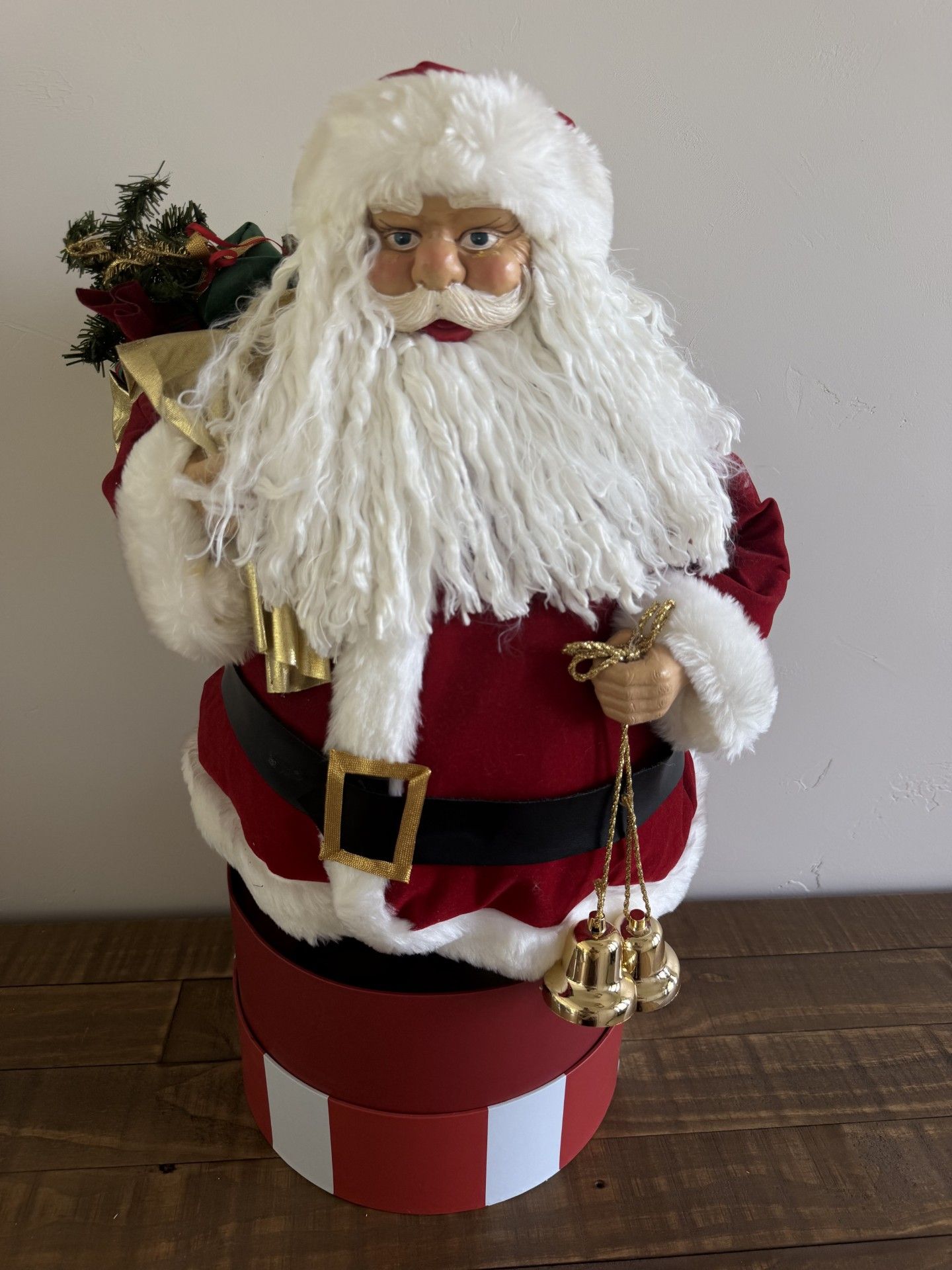 Santa figurine with white beard, red suit, gold bells, and a toy sack on a red-and-white base