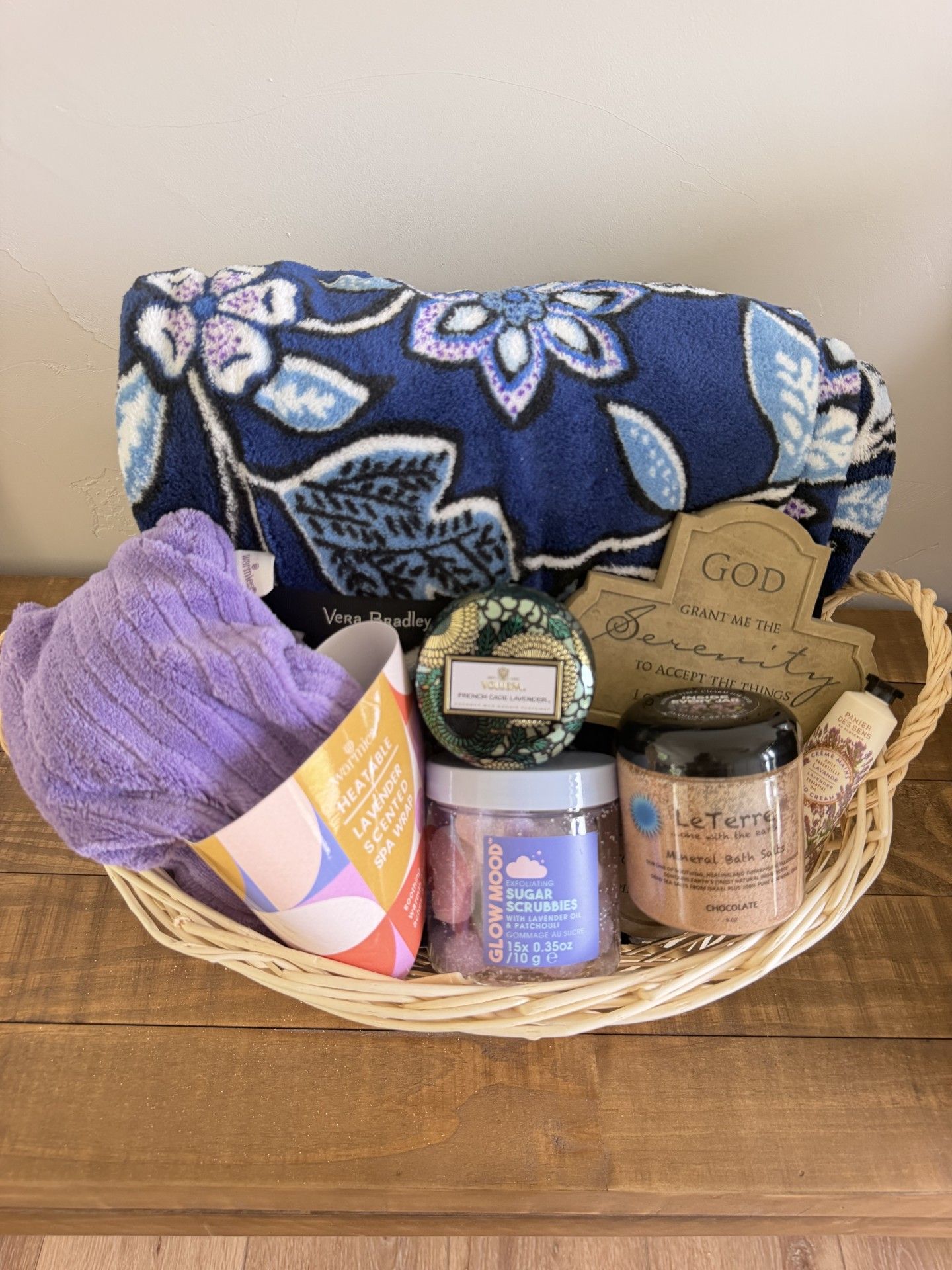 Gift basket with purple blanket, candles, soaps, and a blue floral fabric backdrop.
