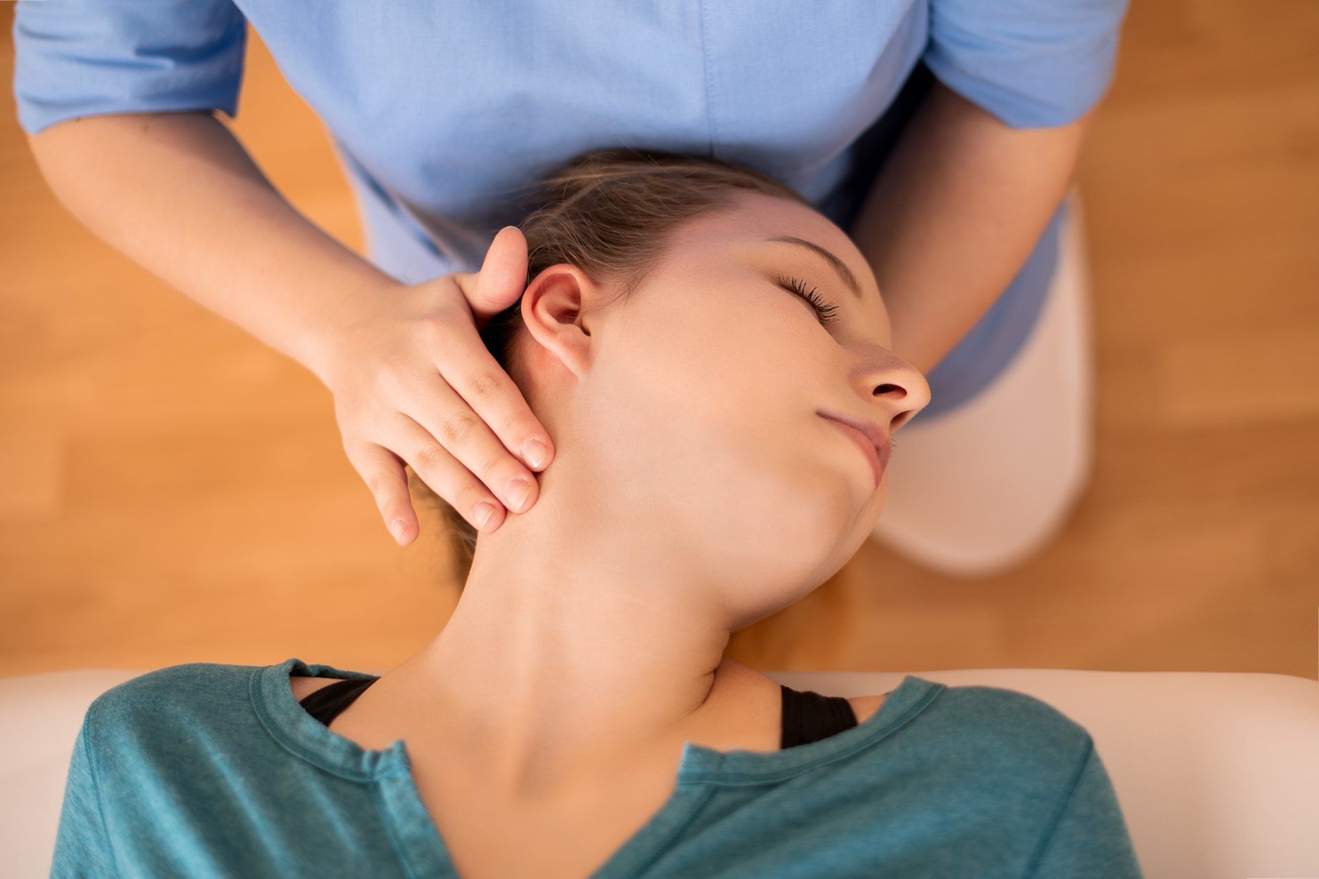 Une femme reçoit un massage du cou par une personne portant une chemise bleue, à l'intérieur.