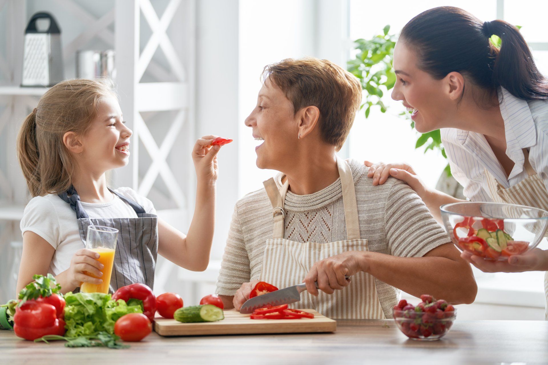 Trois générations de femmes rient en préparant des légumes dans une cuisine.