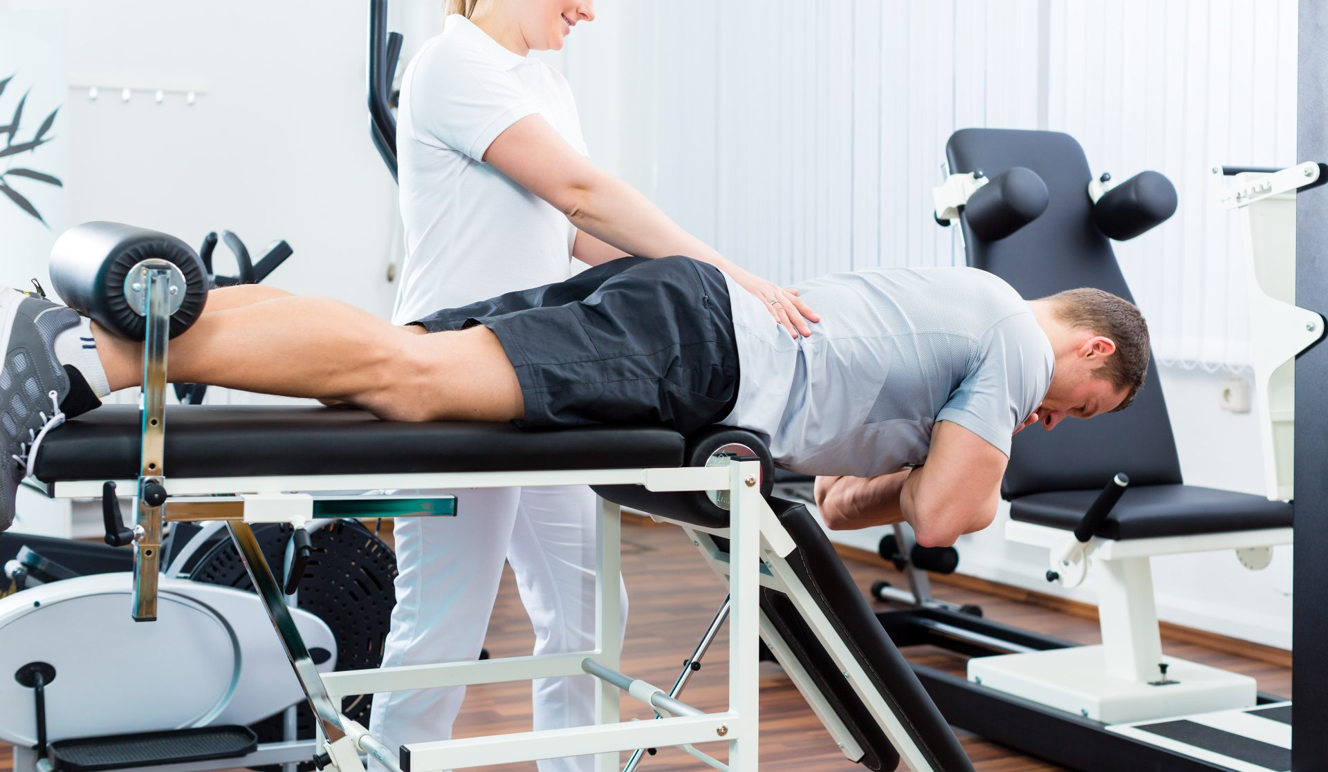 Une femme aide un homme sur une table de rééducation dans une clinique de physiothérapie.