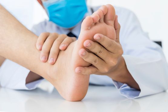 Doctor examining a patient's foot; doctor is wearing a face mask and white coat.