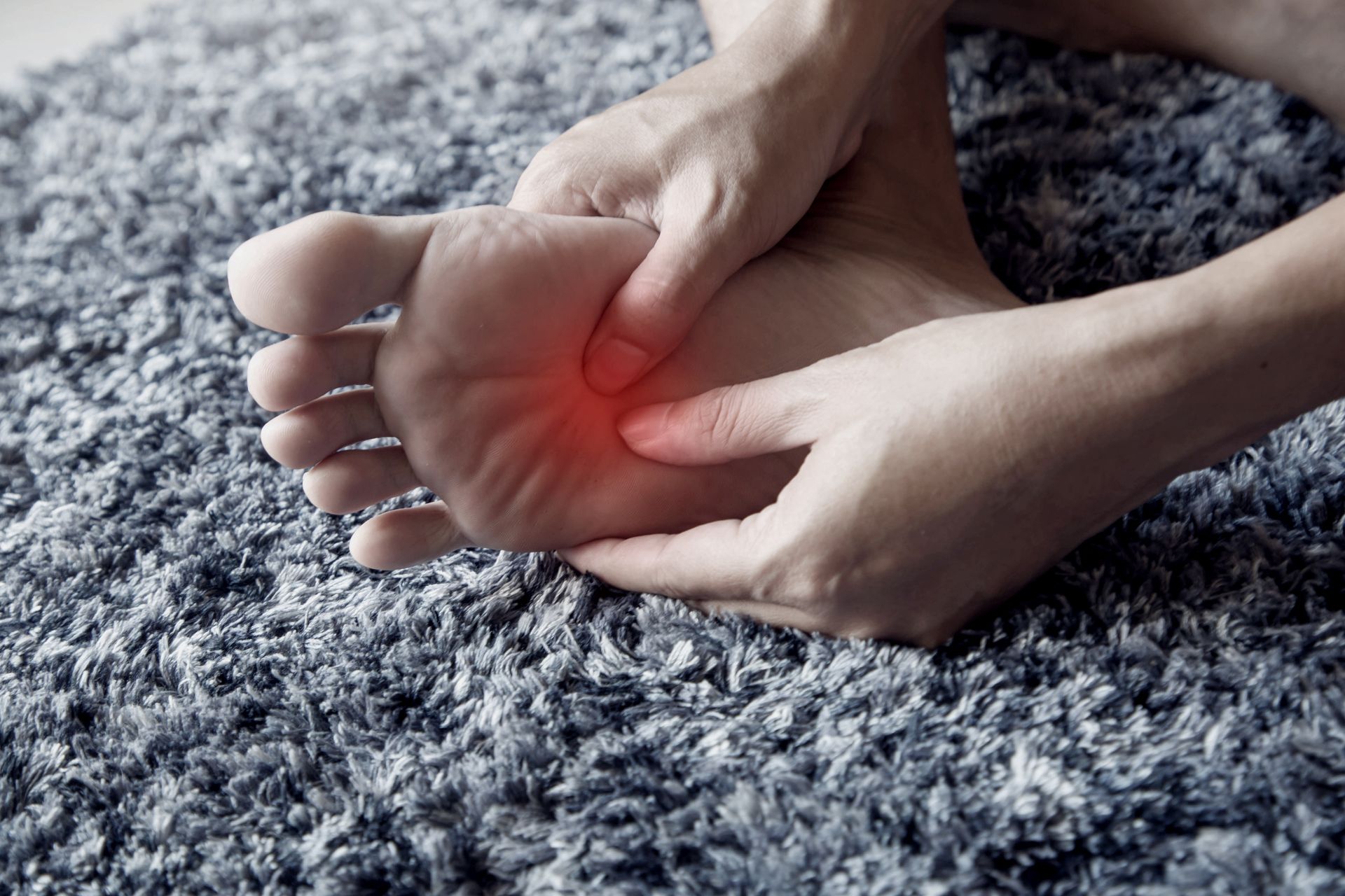 Person's foot being massaged, showing red indication of pain on the sole, against a gray carpet.