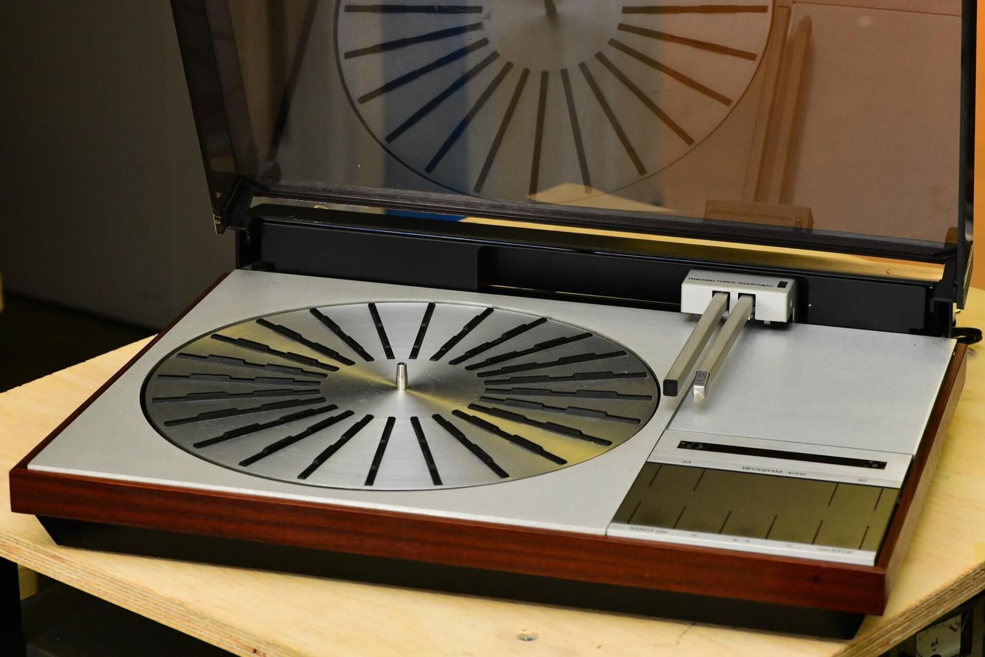 Vintage turntable with clear dust cover open, showing a silver platter and tonearm on a wooden base