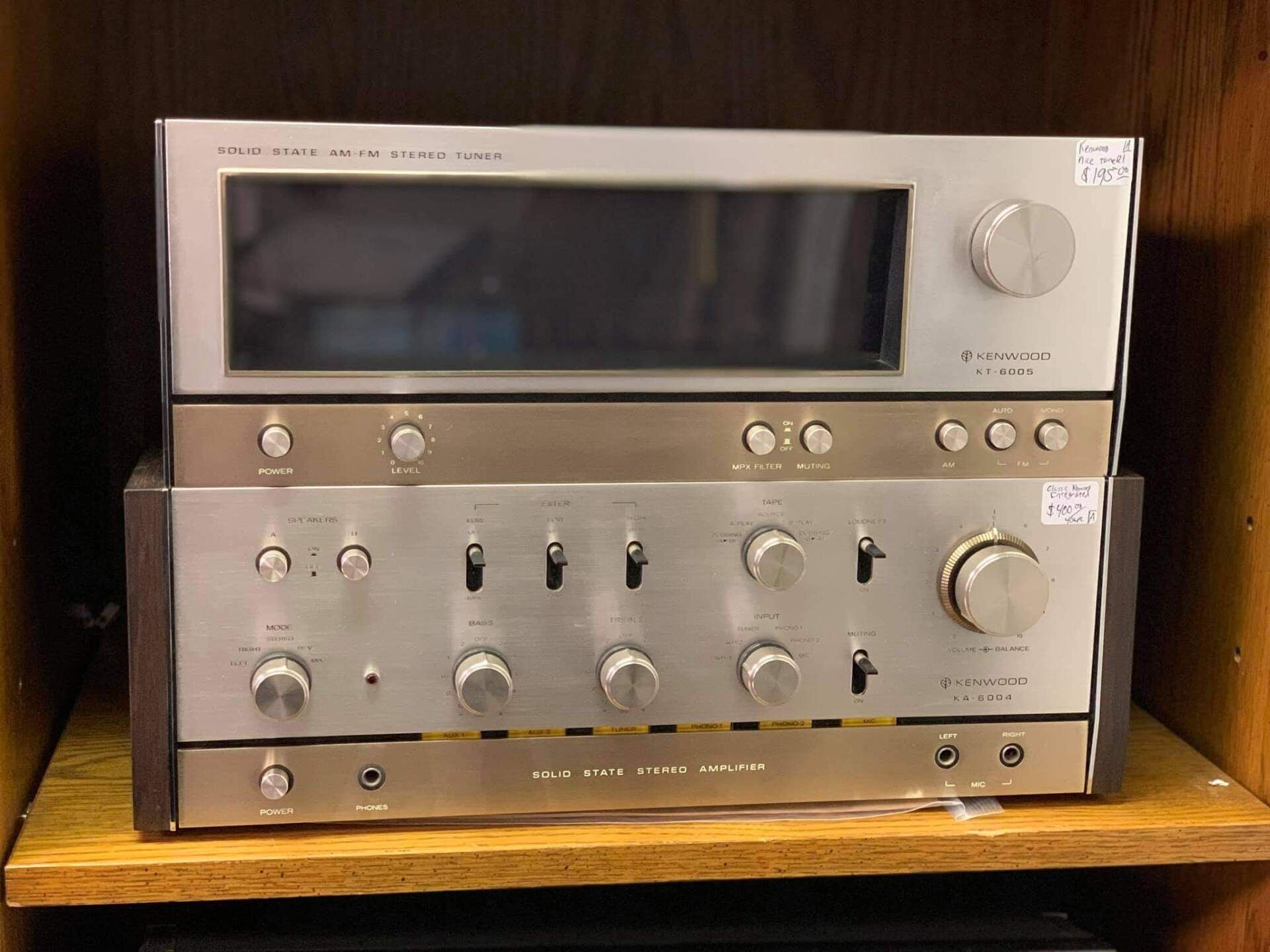 Two stacked silver stereo components on a wooden shelf with large knobs and dials
