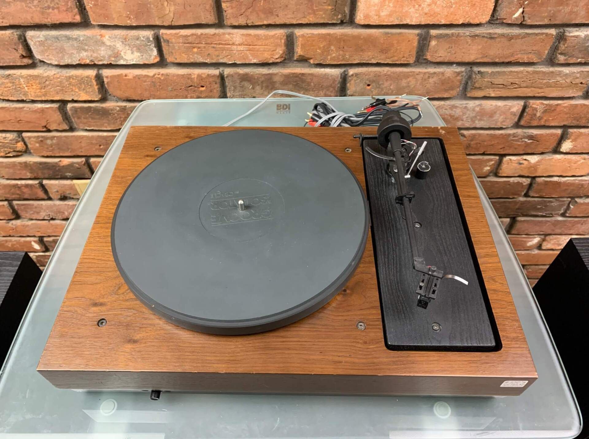 Vintage turntable with gray platter and tonearm on a wood base against a brick wall