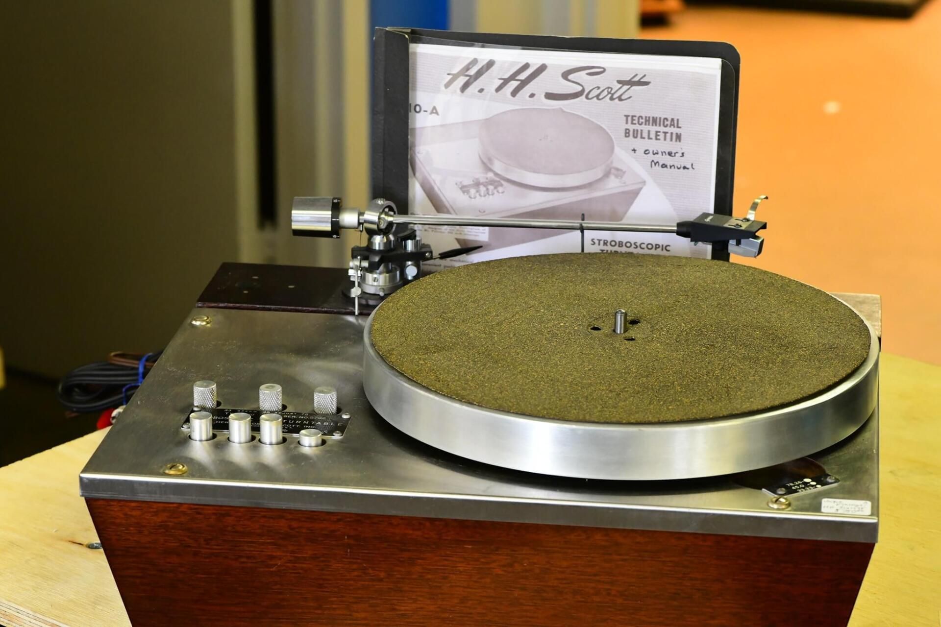 Close-up of a vintage turntable record player with a platter, controls, and a display card behind it.