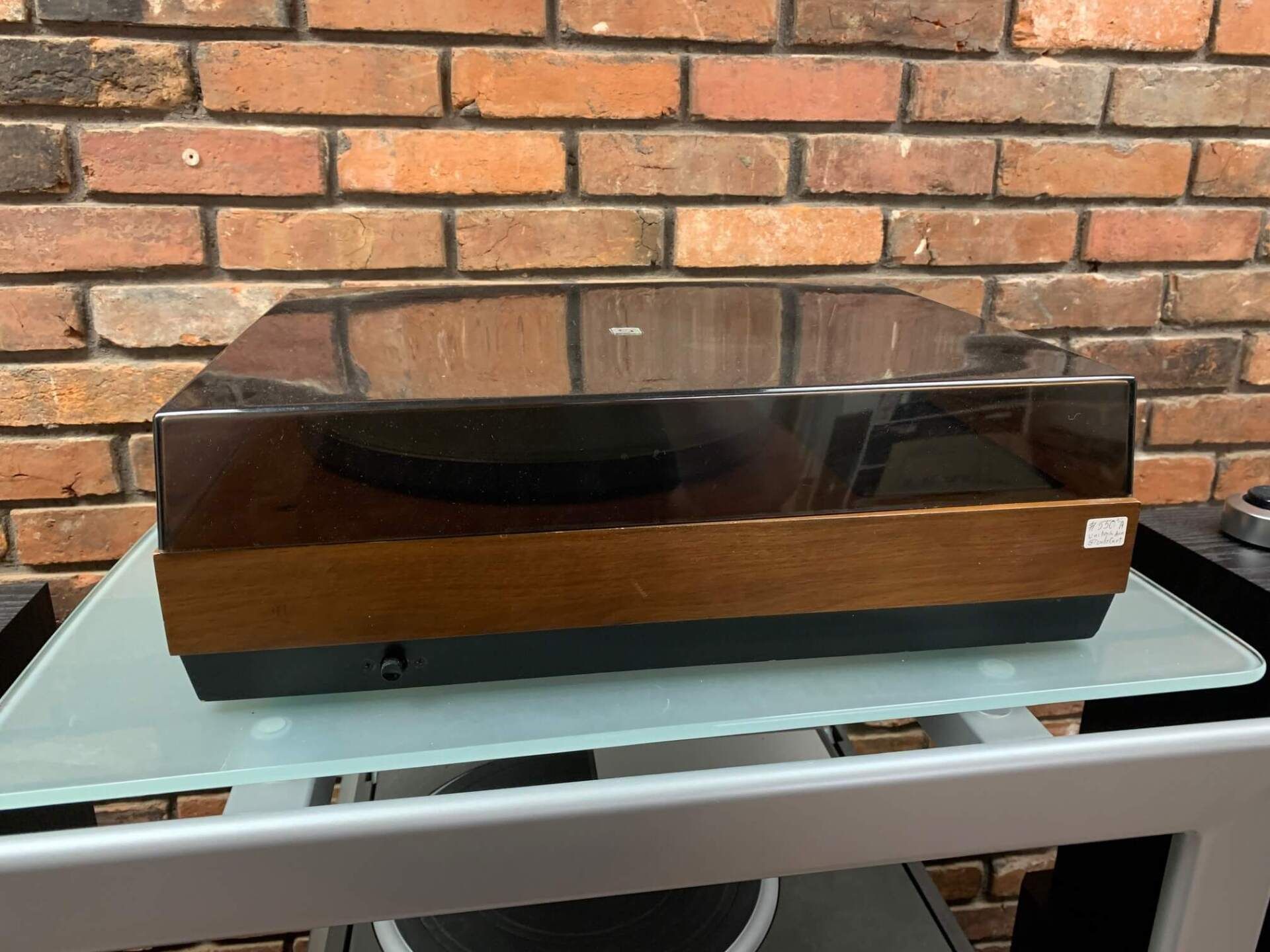 Black turntable on a glass table against a brick wall.
