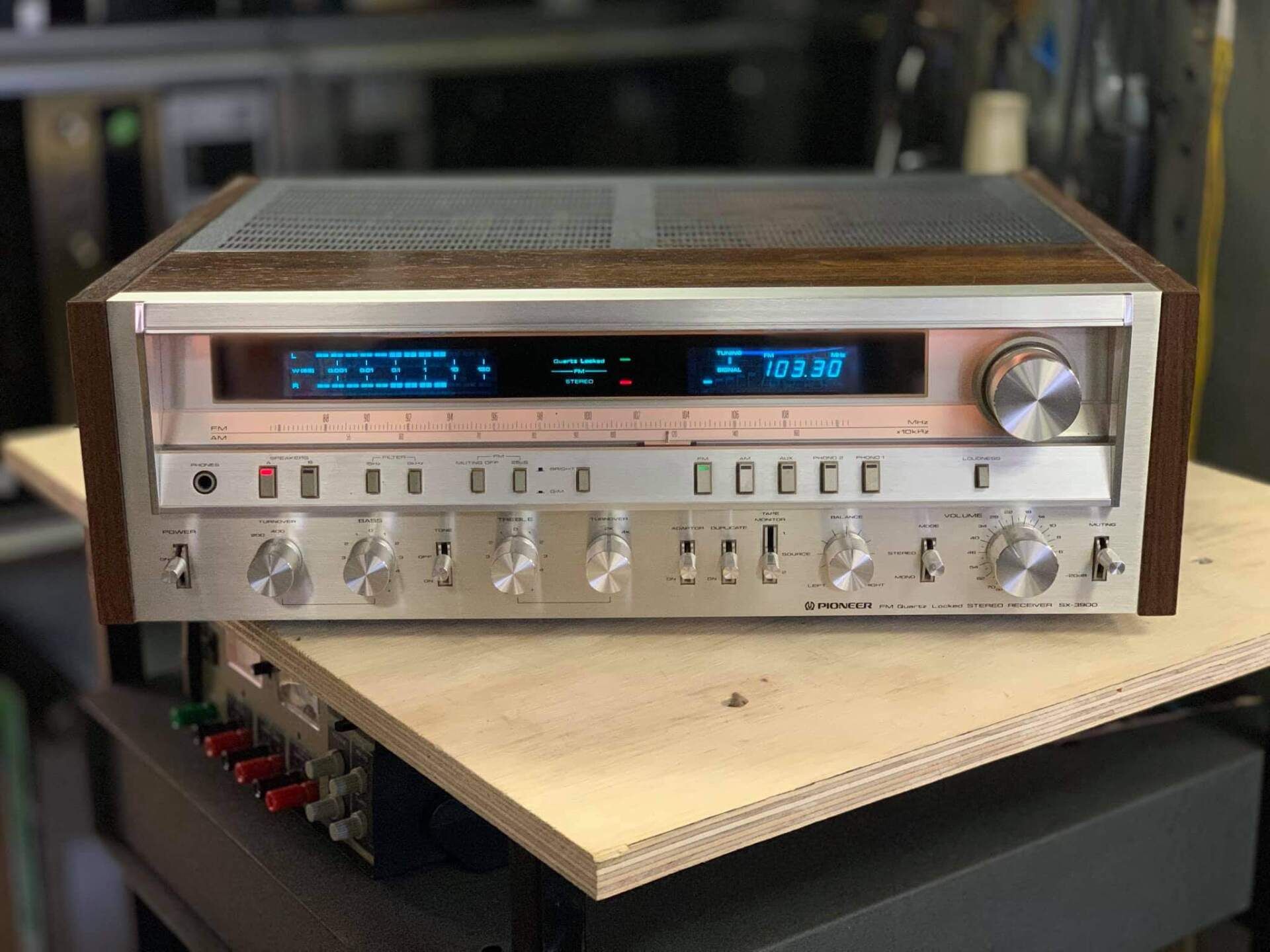Vintage silver stereo receiver with blue-lit display and many knobs on a wooden surface