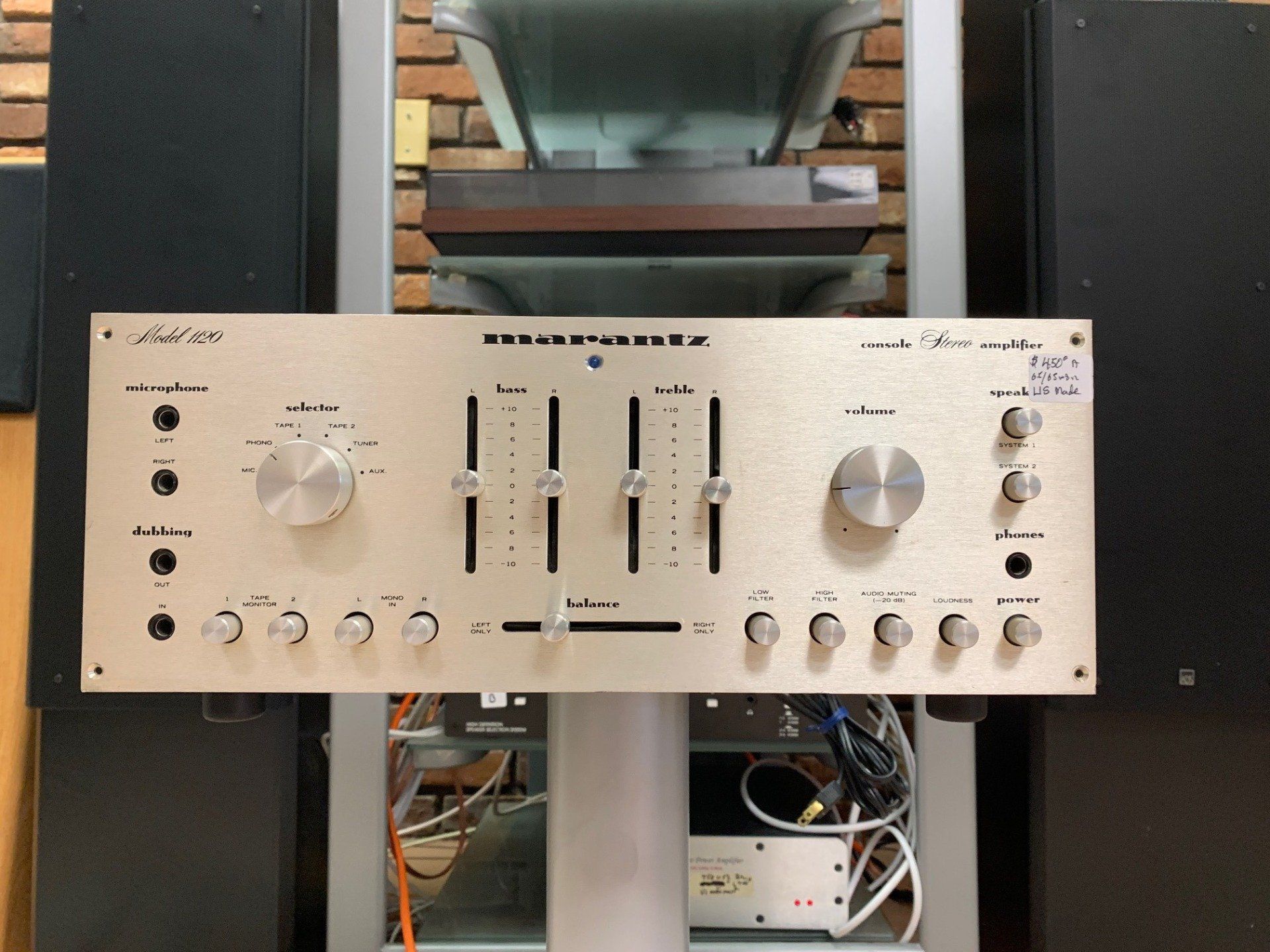 Vintage silver audio amplifier with knobs and sliders on a shelf in front of stereo equipment.