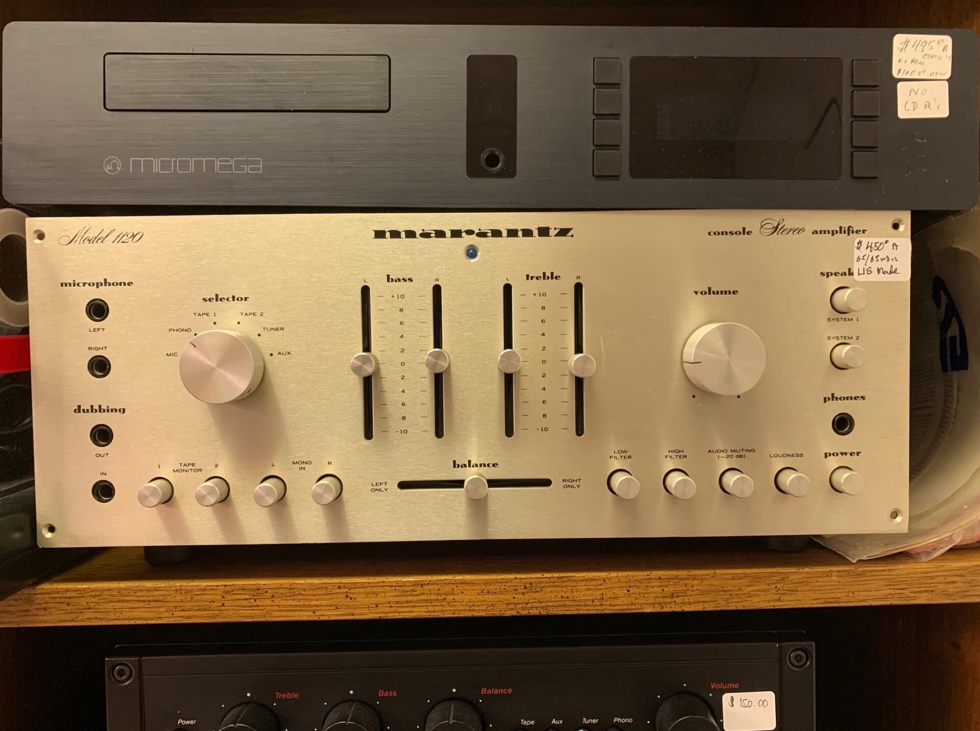 Stacked audio components: black and silver stereo receivers with knobs and sliders on a shelf.
