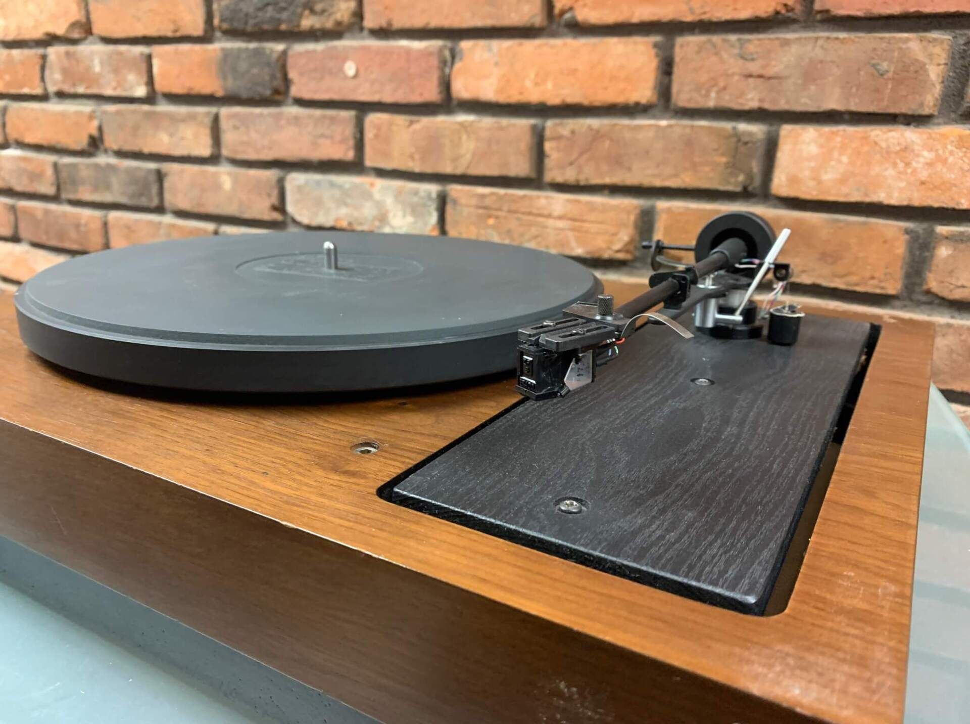 Vintage turntable on a wooden cabinet against a brick wall.