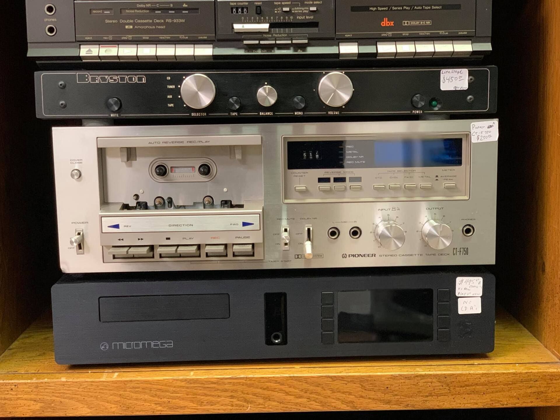 Stacked vintage audio components on a wooden shelf, including cassette decks and silver stereo equipment.
