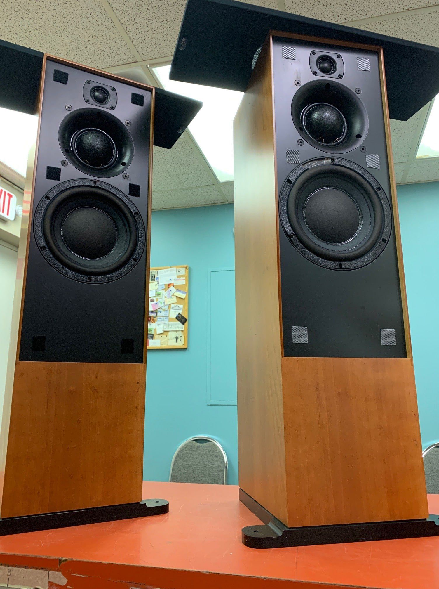Two black floor-standing speakers with wood bases on a table in a room.