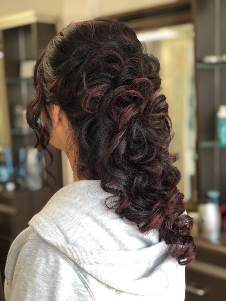 A woman with long curly hair is wearing a gray hoodie.