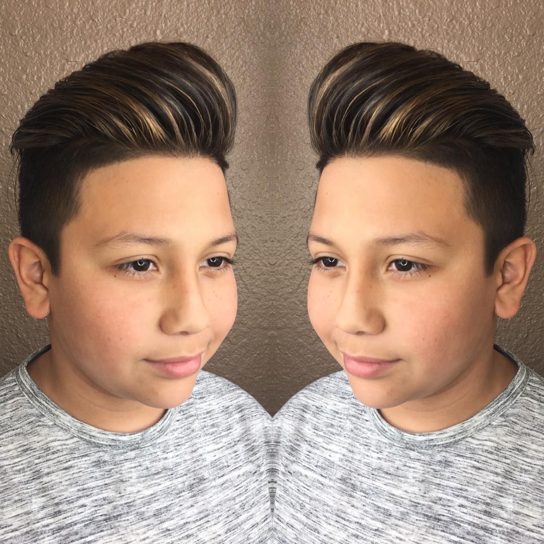 A young boy is wearing a gray sweater and has his hair in a pompadour.