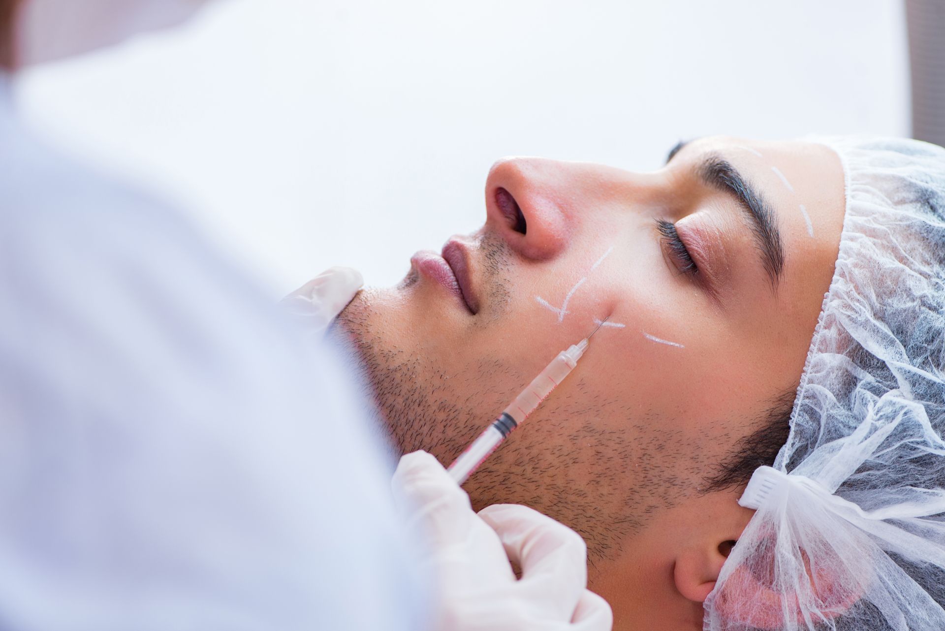 Cosmetic injection into a man’s cheek while lying down in a clinic setting