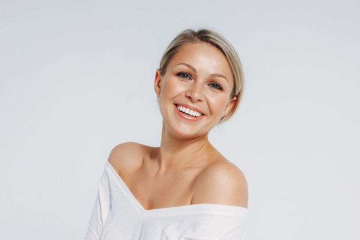Smiling blonde woman in a white off-shoulder top against a light gray background