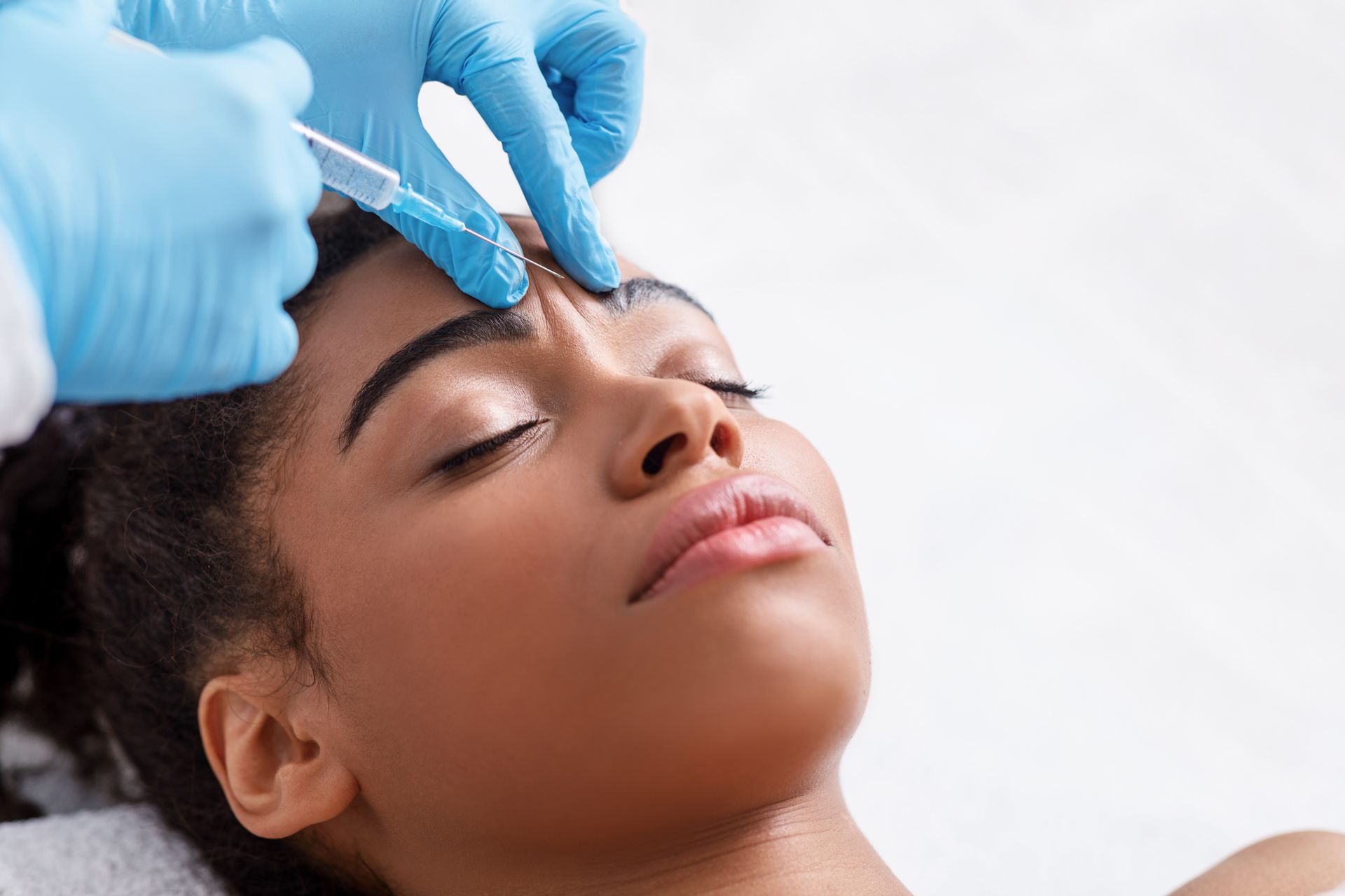 Gloved hands applying eyebrow treatment to a relaxed person lying down