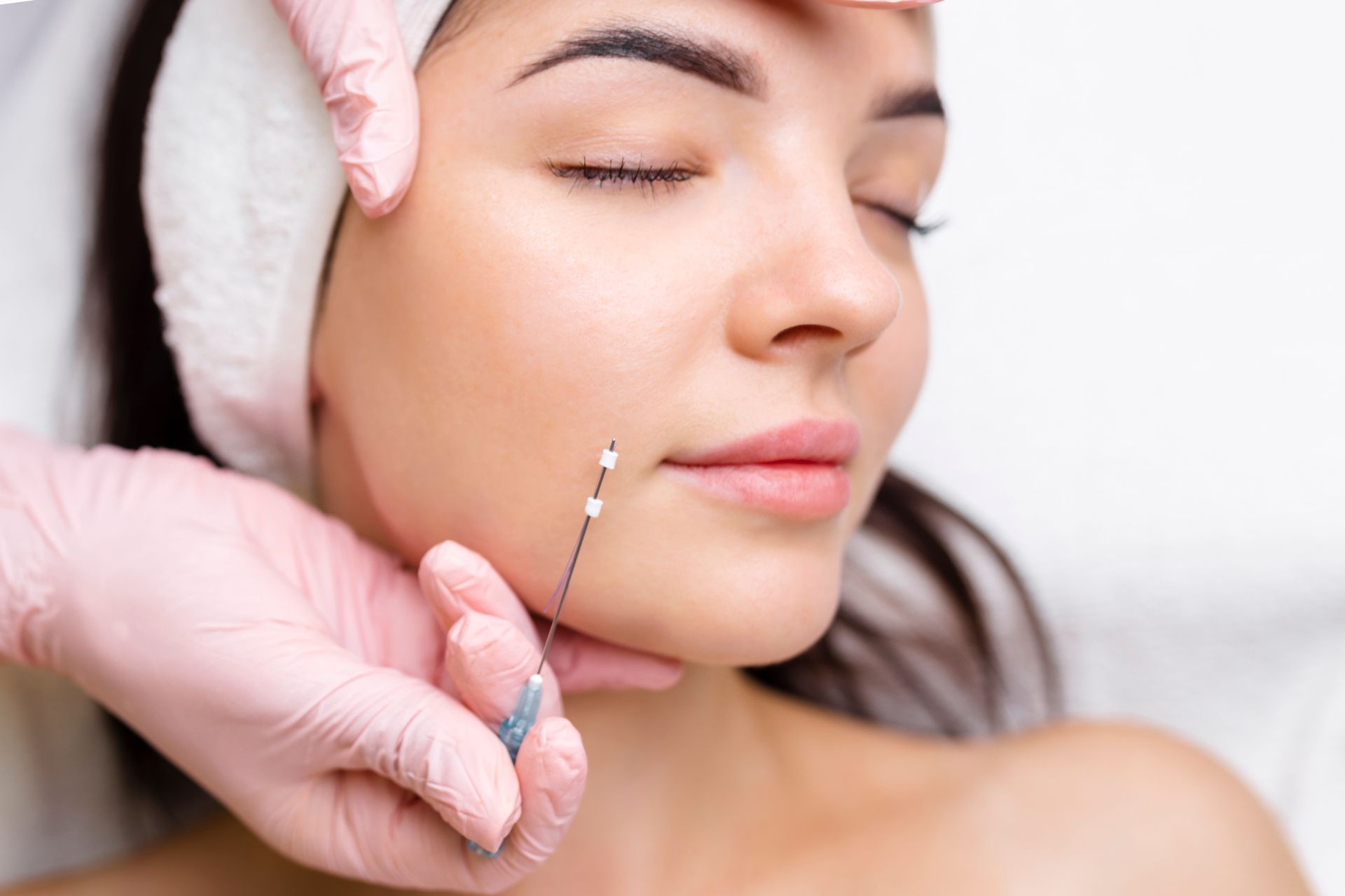 Cosmetologist applying facial treatment with a syringe to a woman’s cheek while another hand steadies her forehead
