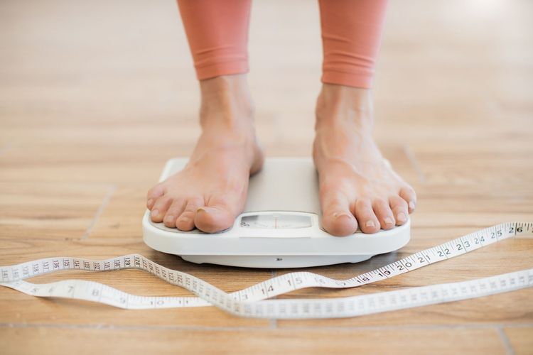 Feet on a white scale with measuring tape on a wooden floor