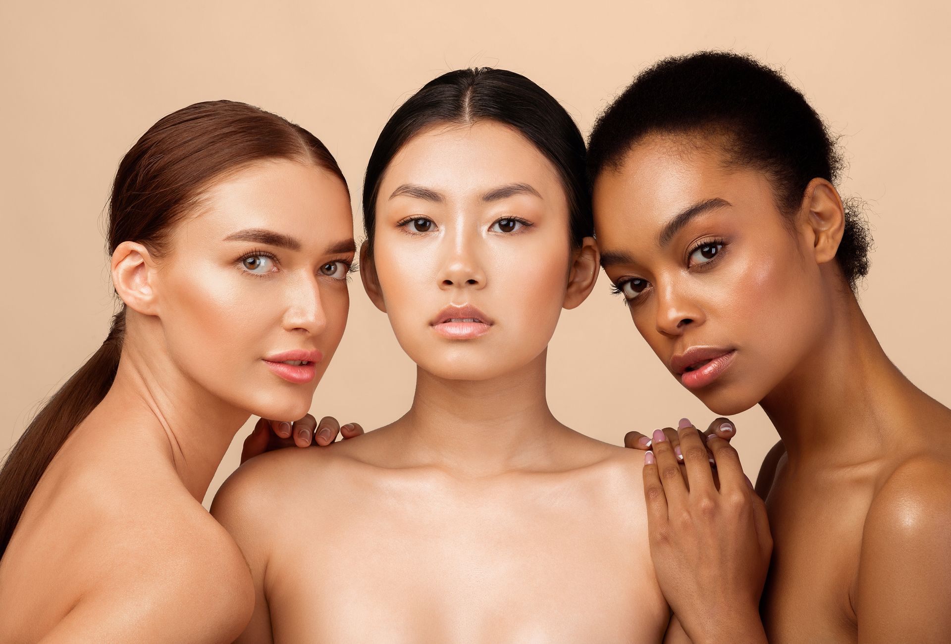 Three women posing shoulder to shoulder against a beige background, looking directly at the camera.