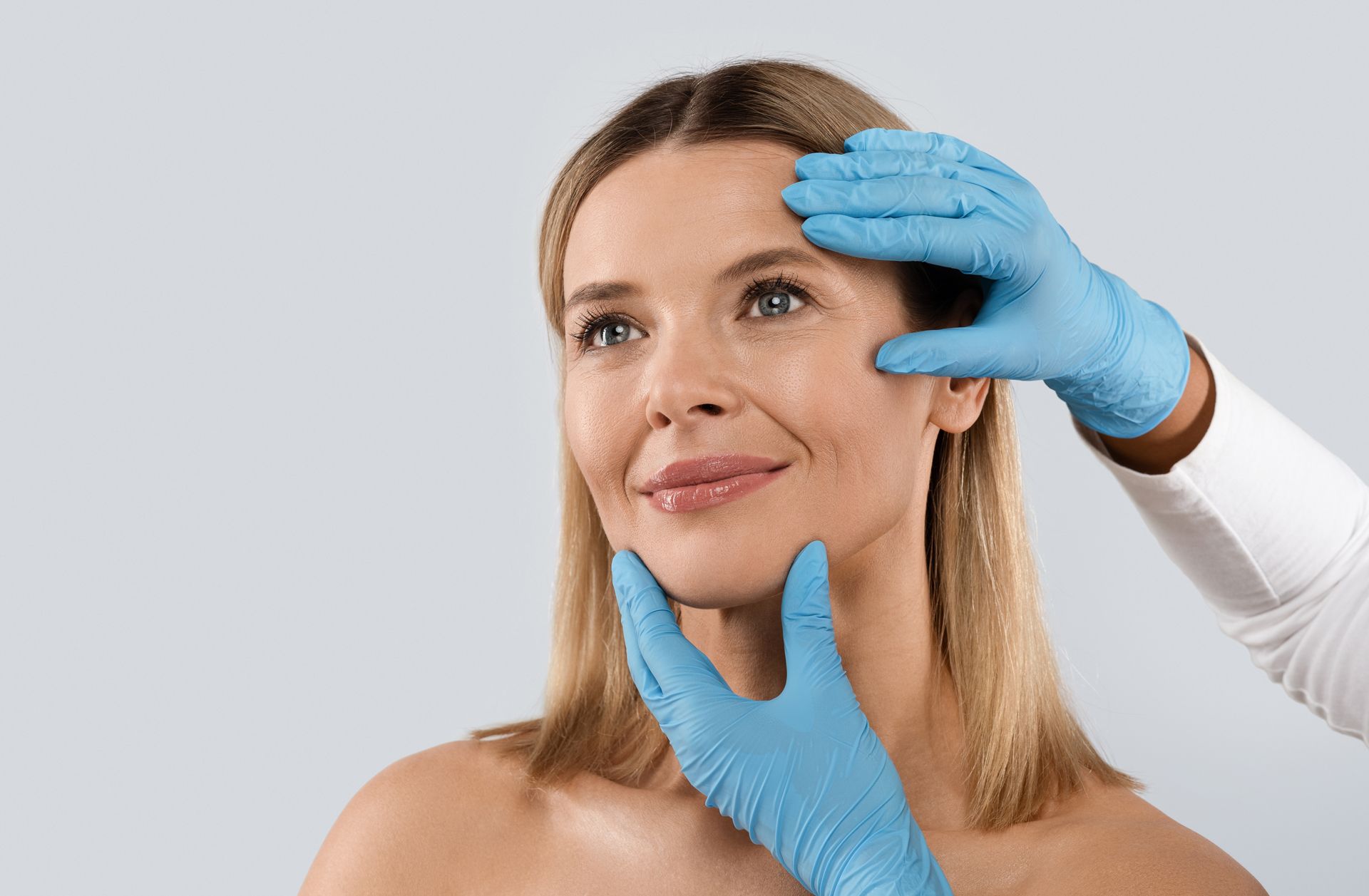 Gloved hands framing a woman’s face during a cosmetic consultation